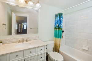 Full downstairs bathroom featuring shower / bath combination with curtain, vanity, and toilet