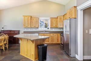 Kitchen featuring light brown cabinets, sink, high vaulted ceiling, stainless steel appliances, and a kitchen breakfast bar