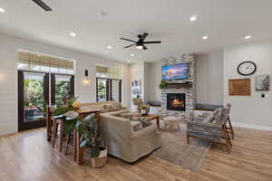 Living room with a brick fireplace, french doors, light wood-type flooring, and ceiling fan