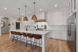 Kitchen featuring premium range hood, hanging light fixtures, a kitchen island with sink, appliances with stainless steel finishes, and light hardwood / wood-style floors