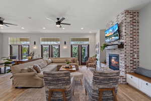 Living room featuring ceiling fan, a brick fireplace, french doors, and light hardwood / wood-style floors