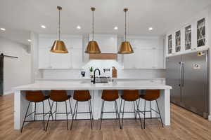 Kitchen featuring a large island with sink, stainless steel appliances, white cabinets, light hardwood / wood-style floors, and a barn door