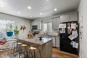 ADU Kitchen featuring light stone counters, gray cabinetry, dark wood-type flooring, black appliances, and a center island