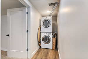 Laundry room with light hardwood / wood-style flooring and stacked washer and dryer