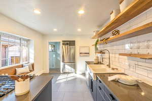 Kitchen featuring dark tile flooring, stainless steel fridge, sink, and tasteful backsplash