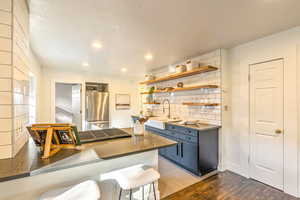 Kitchen featuring dark hardwood floors, stainless steel fridge, sink, kitchen peninsula, and a kitchen breakfast bar