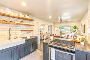 Kitchen, dining and living area with wood flooring, ceiling fan, tasteful backsplash, sink, and stainless steel gas range