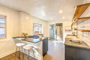 Kitchen featuring stainless steel fridge, a breakfast bar, tile floors, sink, and kitchen peninsula