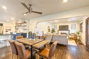 Main level dining/living area with a brick fireplace, ceiling fan, dark wood flooring