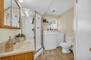 Bathroom with vanity, a shower with shower door, washing machine and dryer, toilet, and a textured ceiling