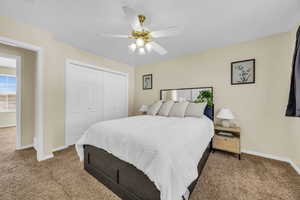 Carpeted bedroom with ceiling fan and a closet