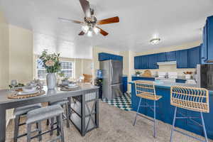 Kitchen with stainless steel fridge, kitchen peninsula, blue cabinets, a kitchen breakfast bar, and electric range