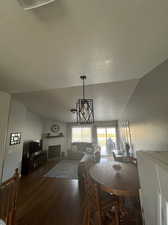 Dining room featuring an inviting chandelier, dark wood-type flooring, vaulted ceiling, a fireplace, and a textured ceiling