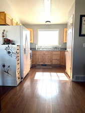 Kitchen with light brown cabinets, white fridge with ice dispenser, a textured ceiling, dark wood-type flooring, and sink