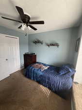 Carpeted bedroom with ceiling fan, a closet, and a textured ceiling