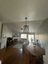 Dining room with dark wood-type flooring, a fireplace, vaulted ceiling, a chandelier, and a textured ceiling