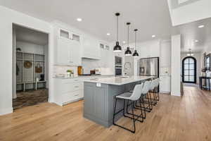 Kitchen with an island with sink, light wood-type flooring, stainless steel appliances, white cabinets, and backsplash