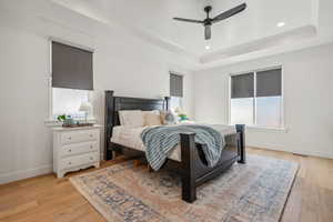 Bedroom with ceiling fan, a tray ceiling, and light hardwood / wood-style floors