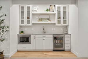 Bar featuring light hardwood / wood-style floors, beverage cooler, stainless steel microwave, sink, and white cabinetry