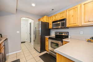 Kitchen featuring a textured ceiling, light tile patterned flooring, stainless steel appliances, and light brown cabinets