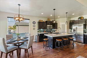 Kitchen featuring pendant lighting, an island with sink, stainless steel appliances, a kitchen breakfast bar, and dark hardwood / wood-style flooring