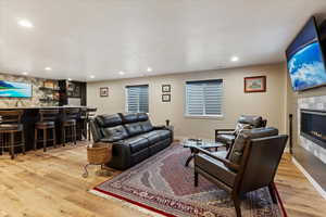 Living room featuring a textured ceiling, a tiled fireplace, bar area, and light hardwood / wood-style flooring