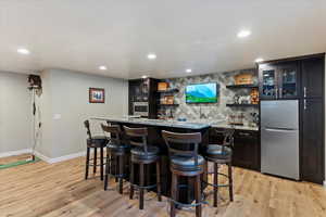 Bar with appliances with stainless steel finishes, light wood-type flooring, light stone countertops, and decorative backsplash