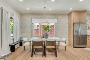 Dining area with light hardwood / wood-style flooring, a textured ceiling, brick wall, and a healthy amount of sunlight