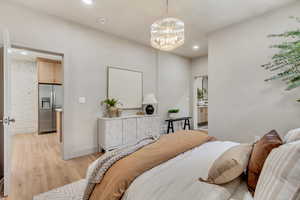 Bedroom with light hardwood / wood-style flooring, stainless steel refrigerator with ice dispenser, a notable chandelier, and ensuite bath