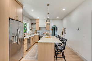 Kitchen with light hardwood / wood-style flooring, light brown cabinets, appliances with stainless steel finishes, and a kitchen island