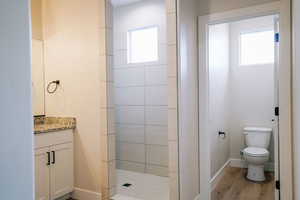 Bathroom featuring hardwood / wood-style flooring, tiled shower, vanity, and toilet