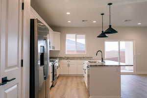 Kitchen with sink, appliances with stainless steel finishes, white cabinetry, light stone counters, and a center island with sink