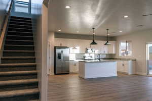 Kitchen with white cabinetry, appliances with stainless steel finishes, wood-type flooring, and decorative light fixtures