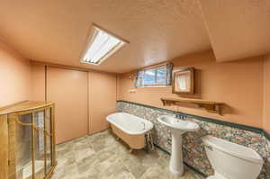 Bathroom featuring a textured ceiling, a bathtub, toilet, and tile walls