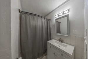 Bathroom with tile walls, vanity, walk in shower, and a textured ceiling