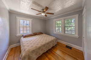 Bedroom with a textured ceiling, ornamental molding, light wood-type flooring, and ceiling fan