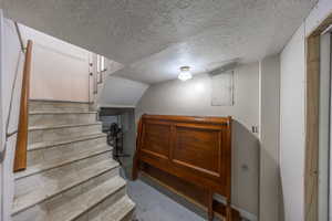 Stairway with electric panel, concrete flooring, and a textured ceiling