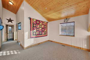 Carpeted empty room with vaulted ceiling and wooden ceiling