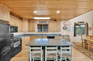 Kitchen with light hardwood / wood-style floors, wood ceiling, black appliances, and sink