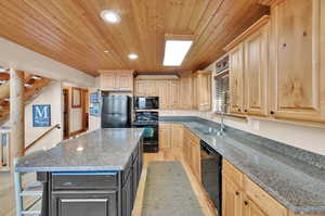 Kitchen with sink, a kitchen island, light hardwood / wood-style flooring, black appliances, and light brown cabinetry