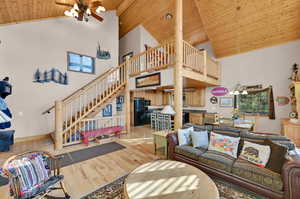 Living room with ceiling fan with notable chandelier, light wood-type flooring, high vaulted ceiling, and wooden ceiling