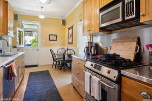 Kitchen with stainless steel counters, stainless steel appliances, sink, ornamental molding, and decorative light fixtures