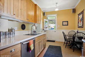 Kitchen with sink, crown molding, hanging light fixtures, light brown cabinetry, and dishwasher