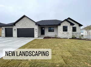 View of front of home with a garage, stone siding, and a front lawn