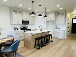 Kitchen with a kitchen island with sink, hanging light fixtures, white cabinetry, and stainless steel appliances