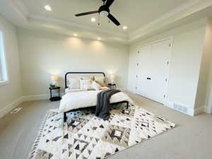 Bedroom featuring a raised ceiling, crown molding, light colored carpet, and ceiling fan