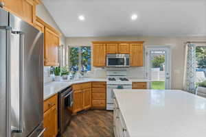 Kitchen featuring tasteful backsplash, dark wood-type flooring, vaulted ceiling, sink, and appliances with stainless steel finishes