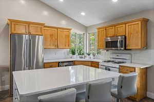 Kitchen with stainless steel appliances, a kitchen island, sink, and vaulted ceiling