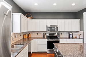 Kitchen with stainless steel appliances, backsplash, sink, and white cabinetry