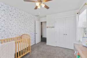 Bedroom featuring light carpet, ceiling fan, a closet, and a crib